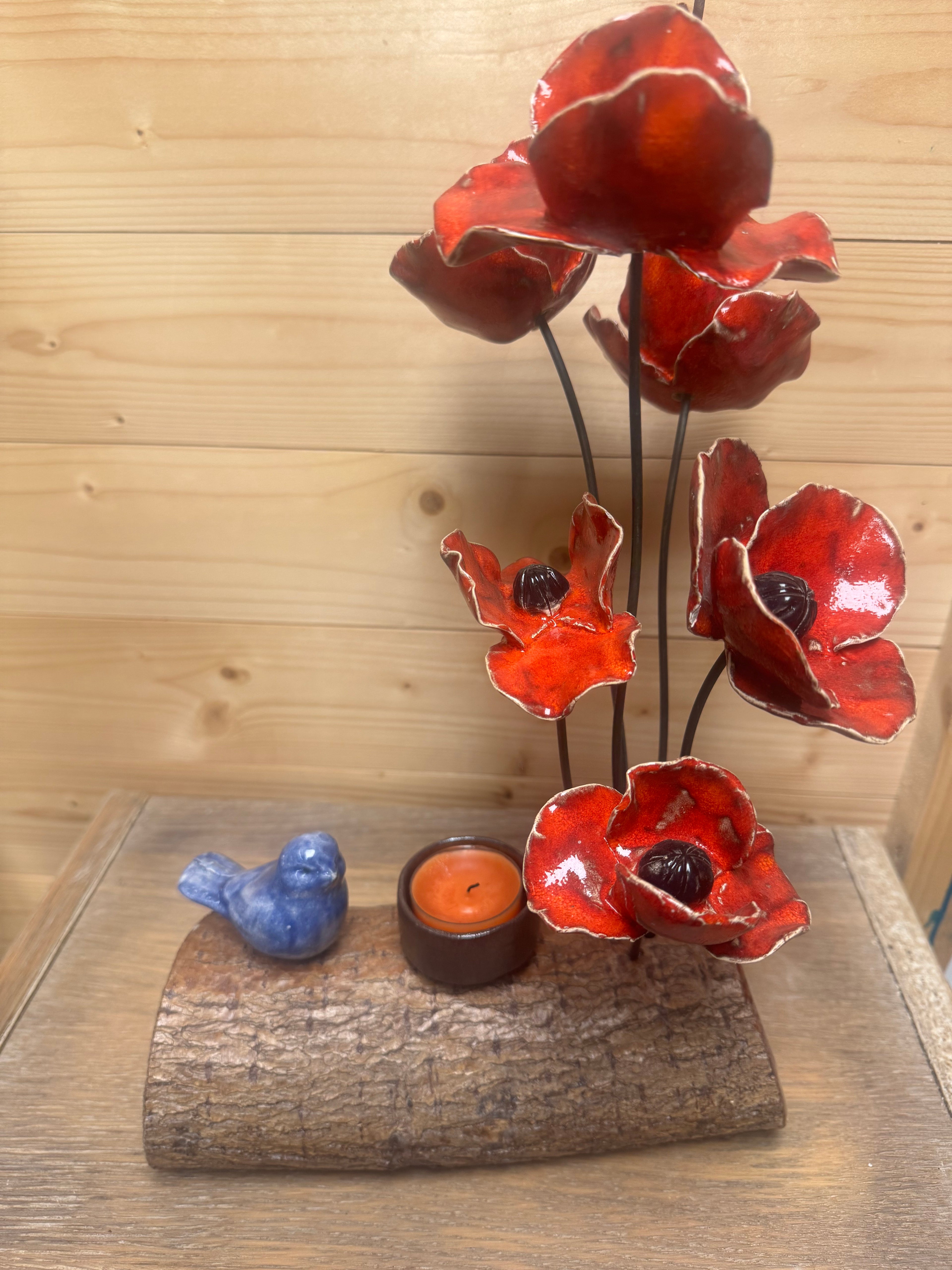 Compositie klaprozen met vogeltje en waxinehouder op een boomstam